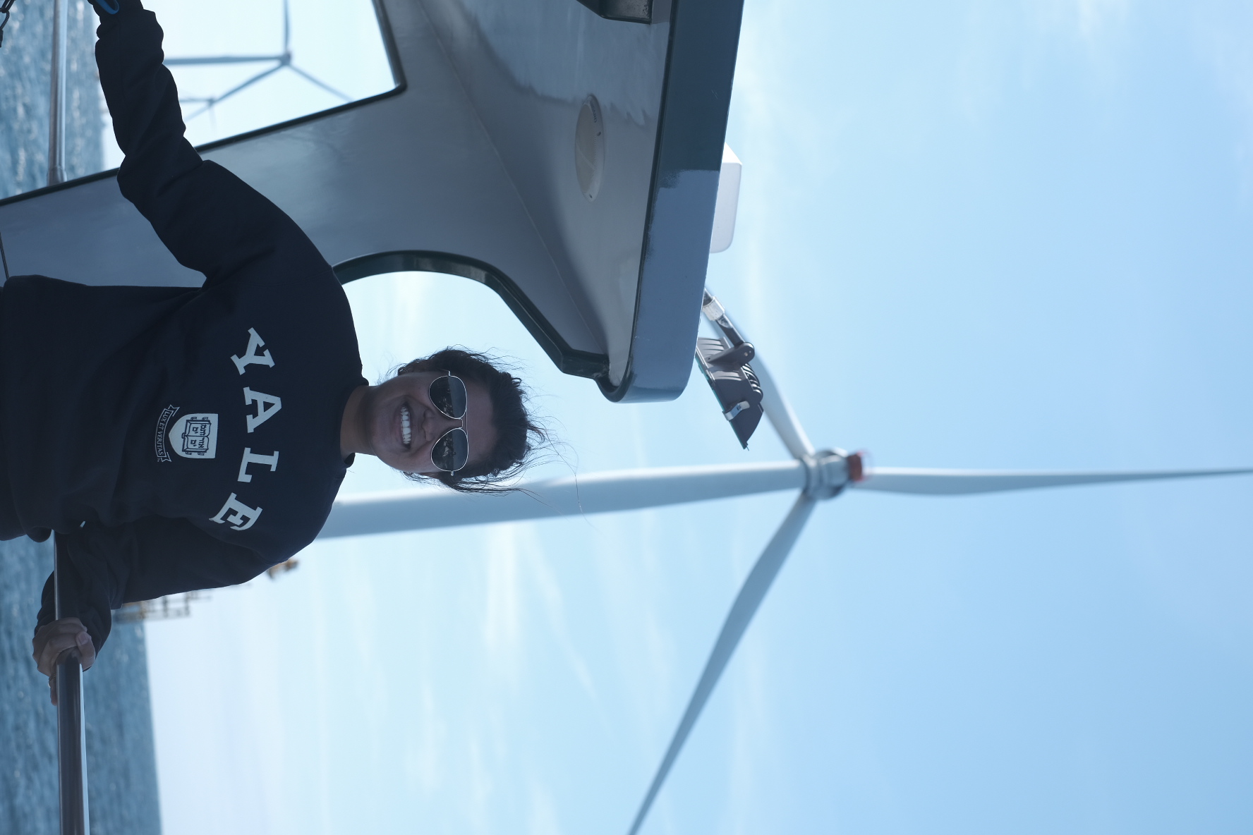 Student wearing a Yale sweatshirt standing in front of an offshore wind turbine